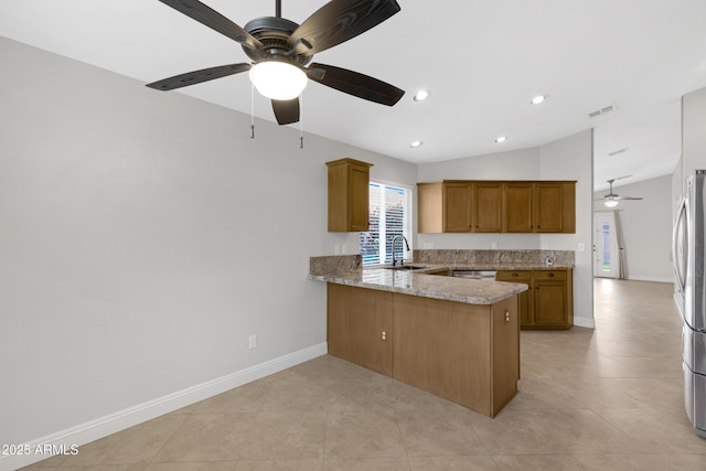 kitchen with lofted ceiling, sink, appliances with stainless steel finishes, kitchen peninsula, and light stone countertops