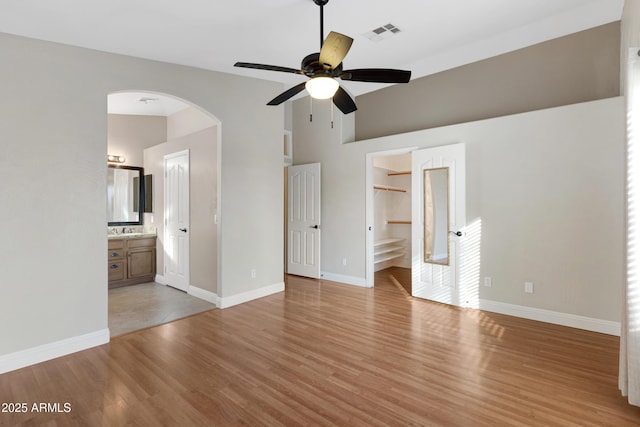 unfurnished bedroom with high vaulted ceiling, sink, light wood-type flooring, and ensuite bath