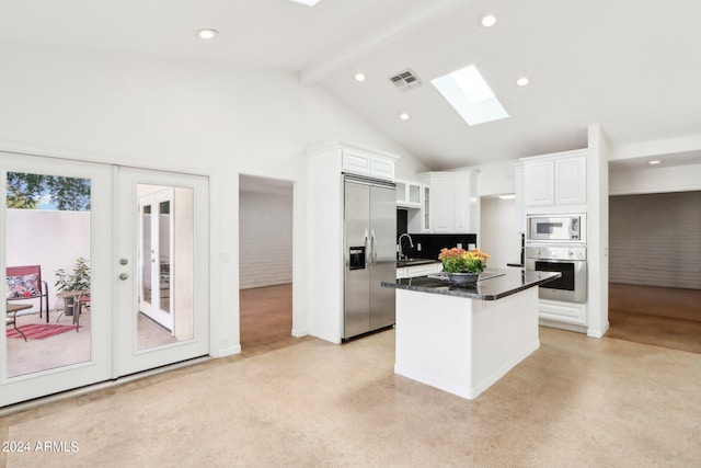 kitchen featuring a kitchen island, beamed ceiling, built in appliances, white cabinetry, and a skylight