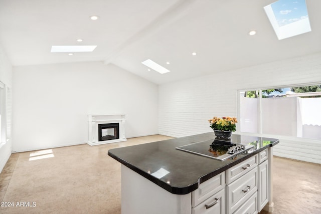 kitchen featuring cooktop, white cabinets, vaulted ceiling with skylight, and a kitchen island