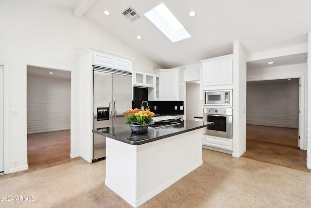 kitchen with a skylight, backsplash, built in appliances, white cabinets, and a center island