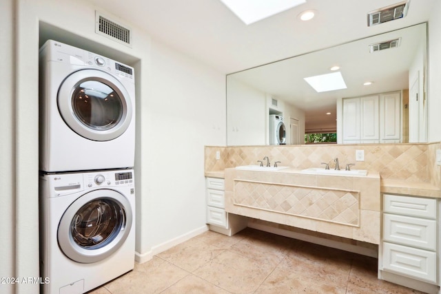 clothes washing area featuring light tile patterned floors, a skylight, stacked washer / dryer, and sink