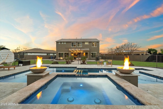 pool at dusk featuring a patio area, an in ground hot tub, and an outdoor fire pit