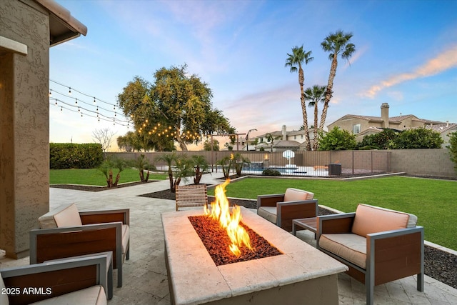 patio terrace at dusk with a fenced in pool, a lawn, and an outdoor living space with a fire pit