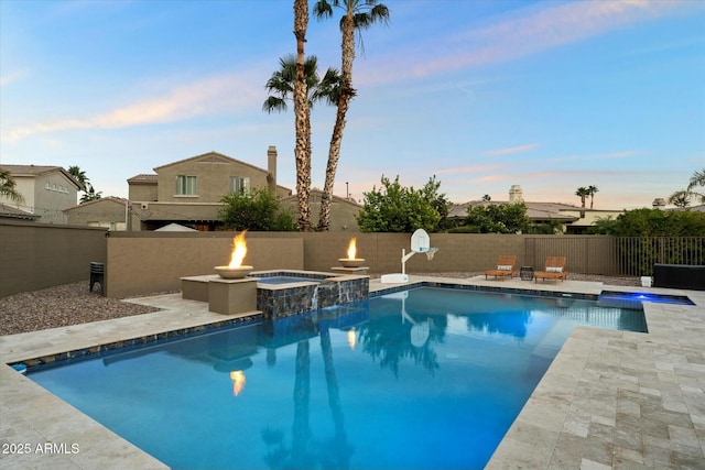 pool at dusk with a fire pit, a patio area, and an in ground hot tub