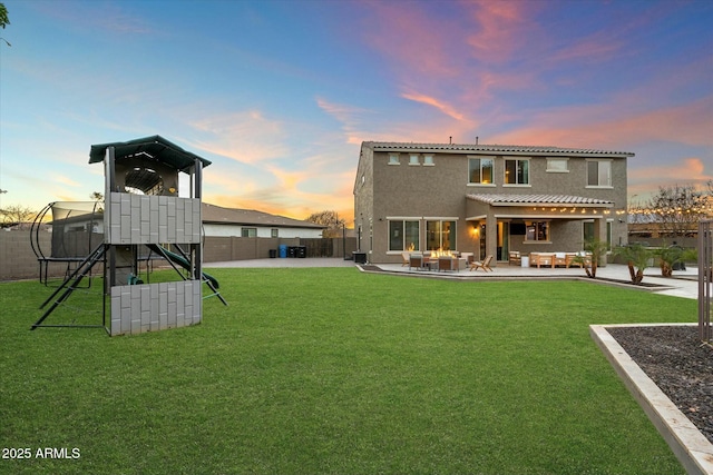 back house at dusk with a yard, an outdoor hangout area, a patio, and a playground