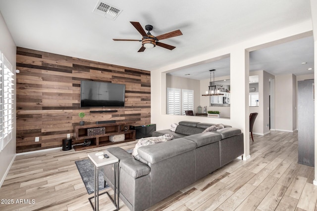 living room with visible vents, light wood-style flooring, an accent wall, a ceiling fan, and wooden walls