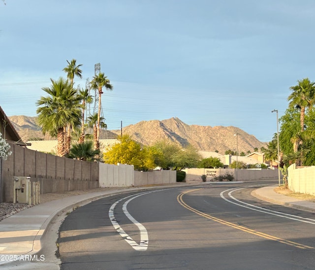 view of asphalt street featuring sidewalks, a mountain view, curbs, and street lighting