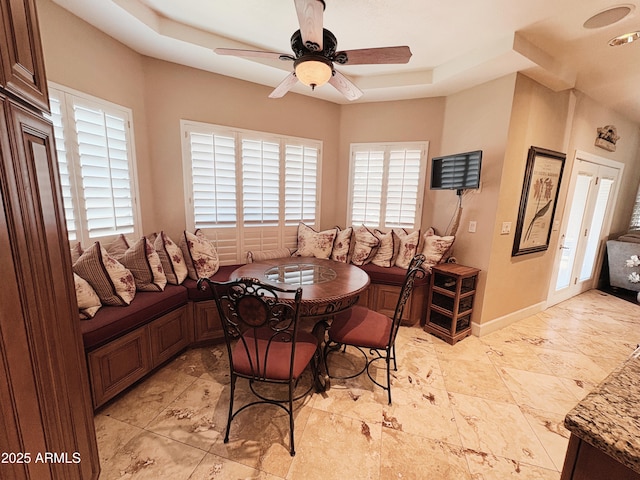 dining space with a tray ceiling, a ceiling fan, and baseboards