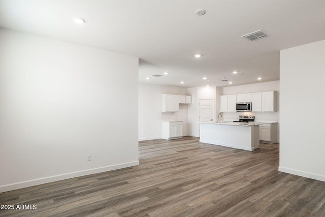 kitchen with sink, appliances with stainless steel finishes, hardwood / wood-style flooring, a kitchen island with sink, and white cabinets