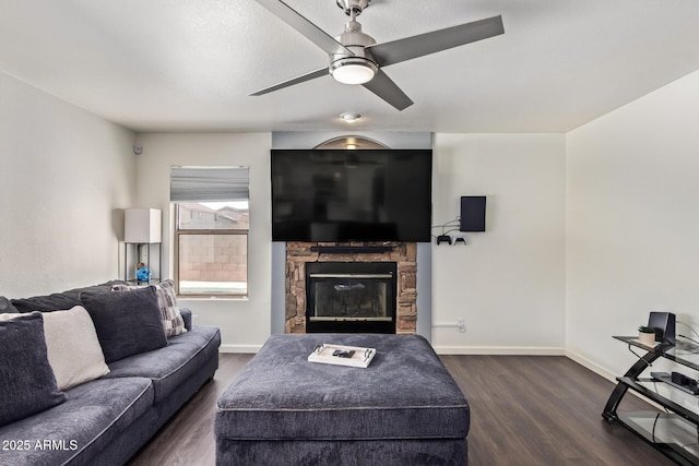 living room featuring dark wood-type flooring, ceiling fan, and a stone fireplace