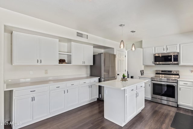 kitchen with appliances with stainless steel finishes, white cabinetry, hanging light fixtures, a kitchen island, and dark hardwood / wood-style flooring