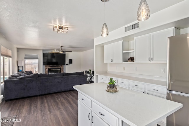 kitchen with a kitchen island, pendant lighting, white cabinets, stainless steel fridge, and dark wood-type flooring