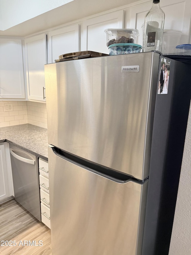 kitchen featuring stone counters, tasteful backsplash, light wood-style flooring, white cabinetry, and stainless steel appliances