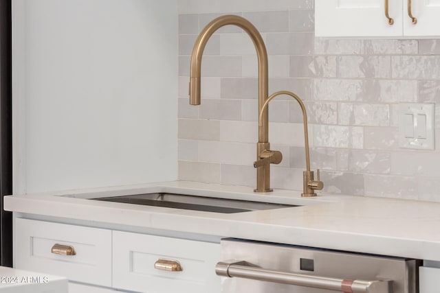 interior details featuring dishwashing machine, light stone counters, white cabinetry, and sink