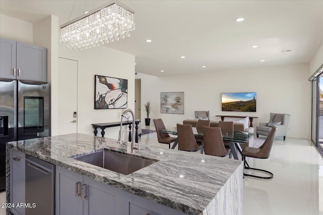 kitchen with light stone countertops, gray cabinetry, sink, stainless steel fridge with ice dispenser, and a kitchen island