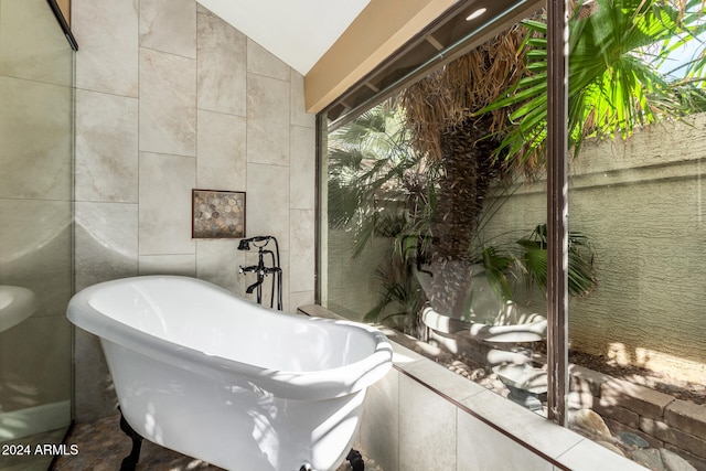 bathroom featuring a tub to relax in, tile walls, and lofted ceiling