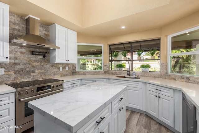 kitchen with stainless steel range, white cabinets, a healthy amount of sunlight, and wall chimney range hood