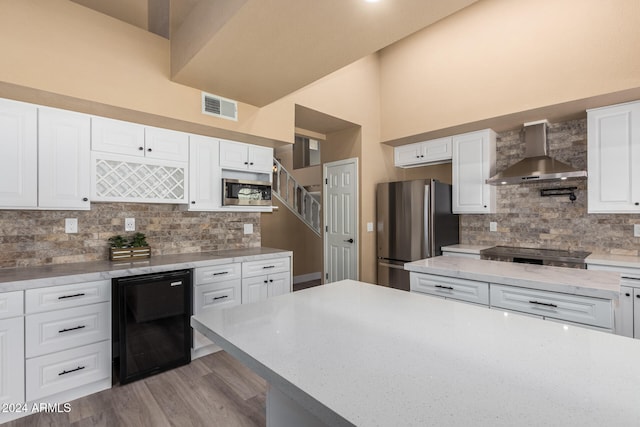 kitchen featuring tasteful backsplash, stainless steel appliances, beverage cooler, wall chimney range hood, and white cabinetry