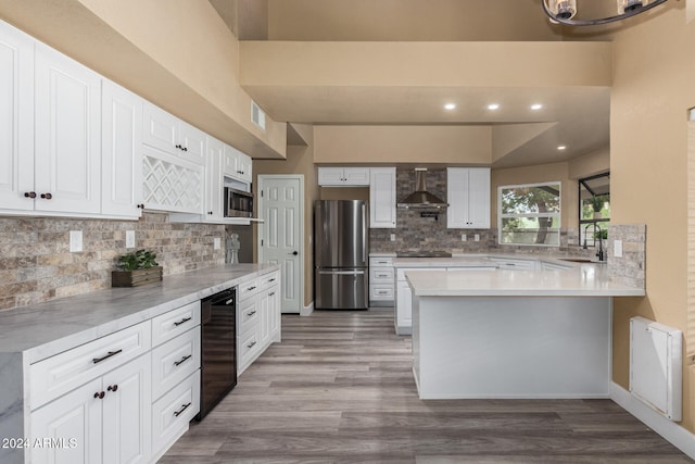 kitchen with white cabinetry, wall chimney range hood, kitchen peninsula, light hardwood / wood-style floors, and appliances with stainless steel finishes