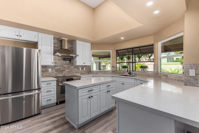 kitchen with white cabinetry, sink, wall chimney range hood, light hardwood / wood-style floors, and appliances with stainless steel finishes