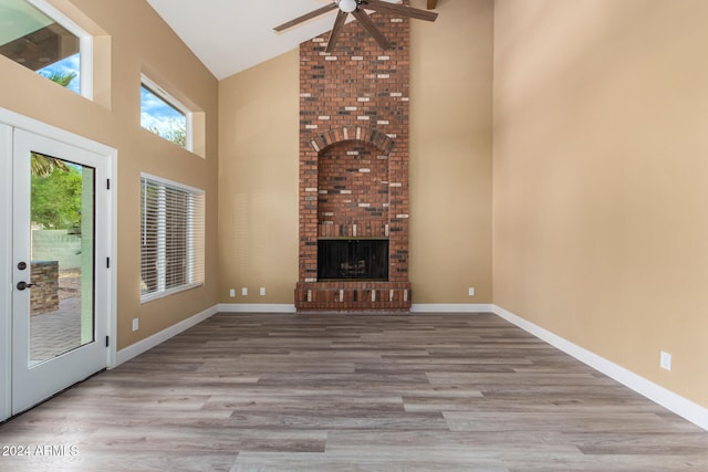 unfurnished living room with a brick fireplace, ceiling fan, high vaulted ceiling, and light hardwood / wood-style flooring