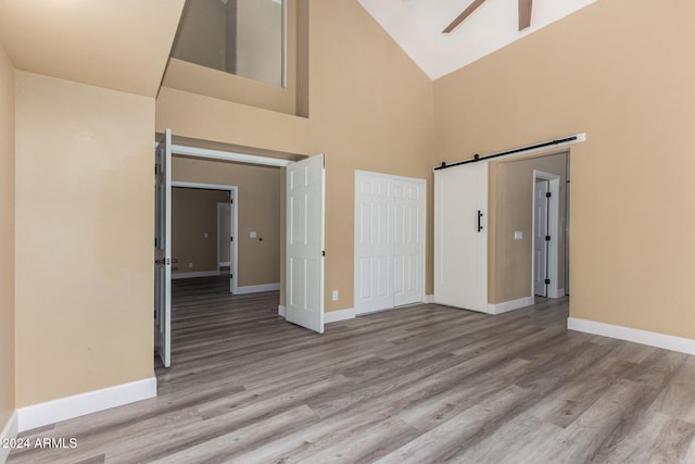 empty room featuring a barn door, ceiling fan, high vaulted ceiling, and light wood-type flooring