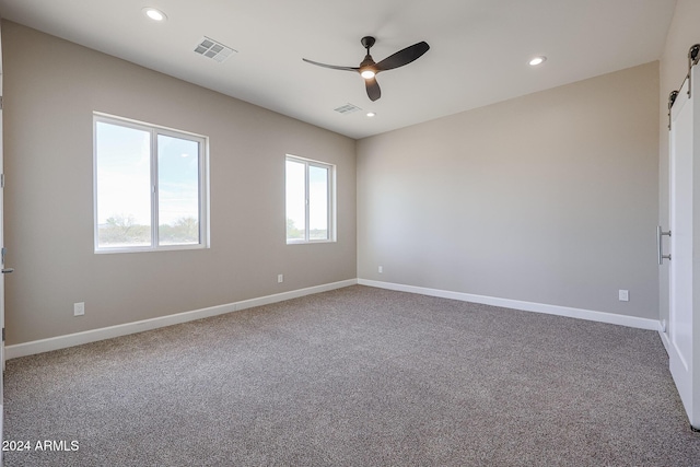 spare room with carpet flooring, a barn door, and ceiling fan