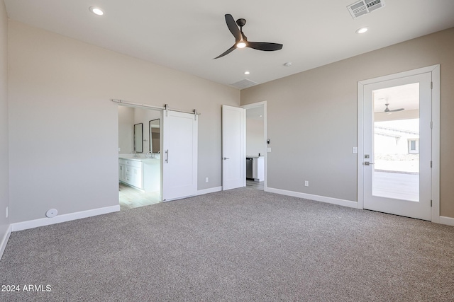 unfurnished bedroom featuring ceiling fan, a barn door, light carpet, and connected bathroom