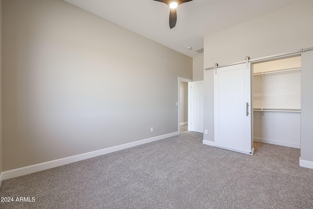 unfurnished bedroom with ceiling fan, a barn door, light carpet, and a closet