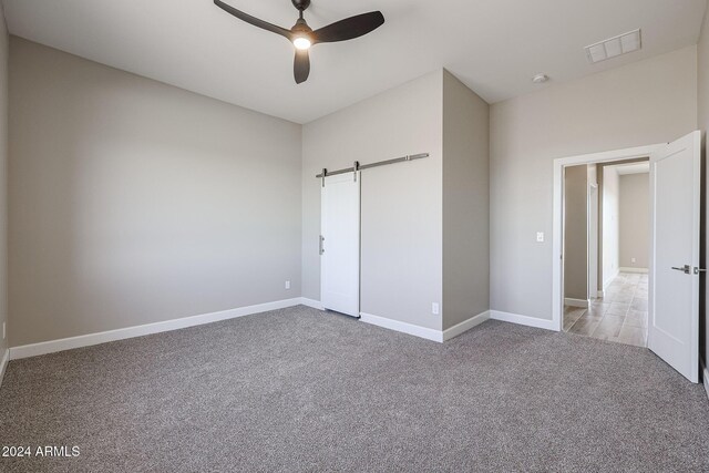 unfurnished bedroom with ceiling fan, a barn door, and light colored carpet