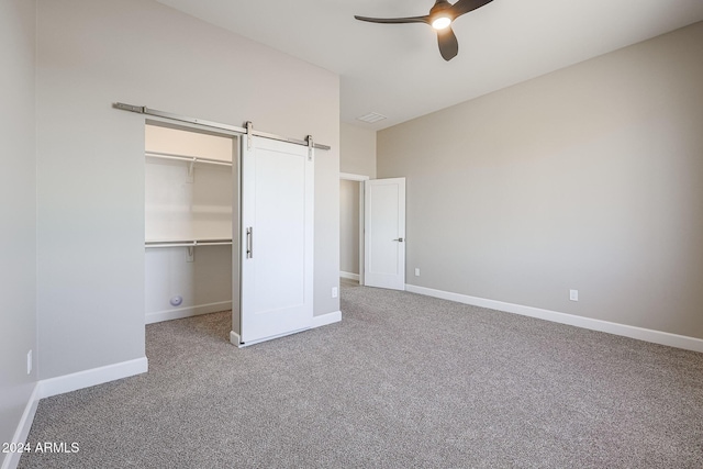 unfurnished bedroom with carpet, ceiling fan, a barn door, a spacious closet, and a closet