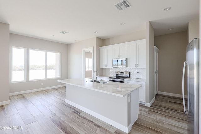 kitchen featuring sink, a kitchen island with sink, decorative backsplash, white cabinets, and appliances with stainless steel finishes