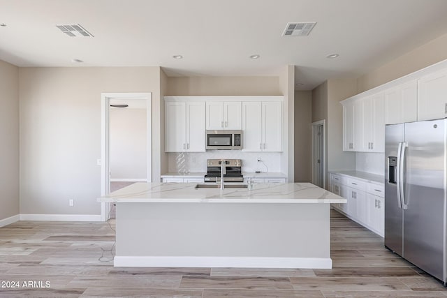 kitchen with a kitchen island with sink, white cabinets, light stone countertops, and appliances with stainless steel finishes