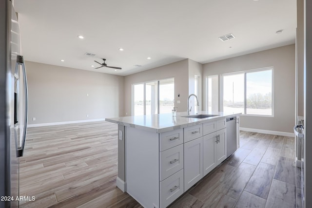 kitchen featuring stainless steel appliances, ceiling fan, sink, white cabinetry, and an island with sink