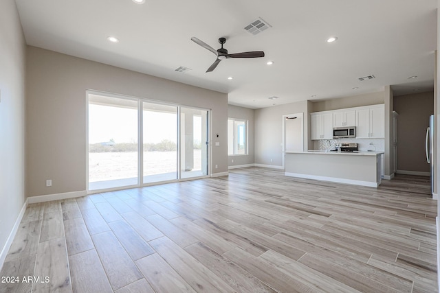 unfurnished living room with ceiling fan, light hardwood / wood-style floors, and a water view