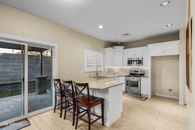 kitchen featuring sink, kitchen peninsula, a kitchen bar, white cabinets, and appliances with stainless steel finishes