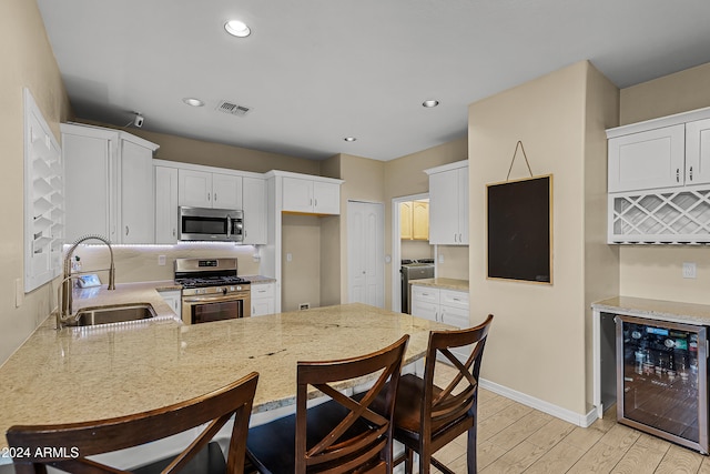 kitchen with sink, stainless steel appliances, wine cooler, kitchen peninsula, and white cabinets