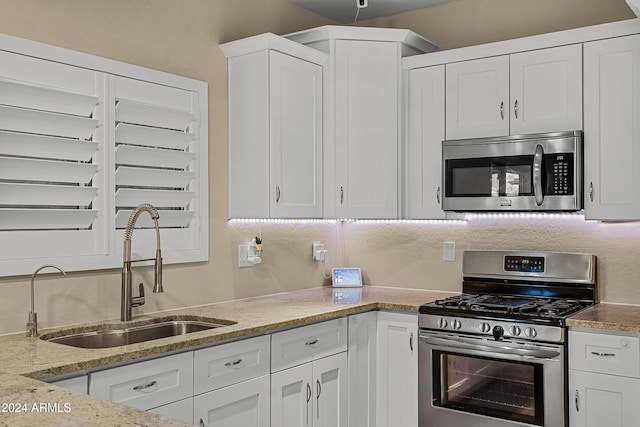 kitchen with appliances with stainless steel finishes, light stone counters, white cabinetry, and sink