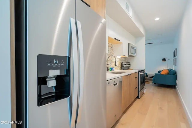 kitchen with a sink, light countertops, appliances with stainless steel finishes, backsplash, and modern cabinets