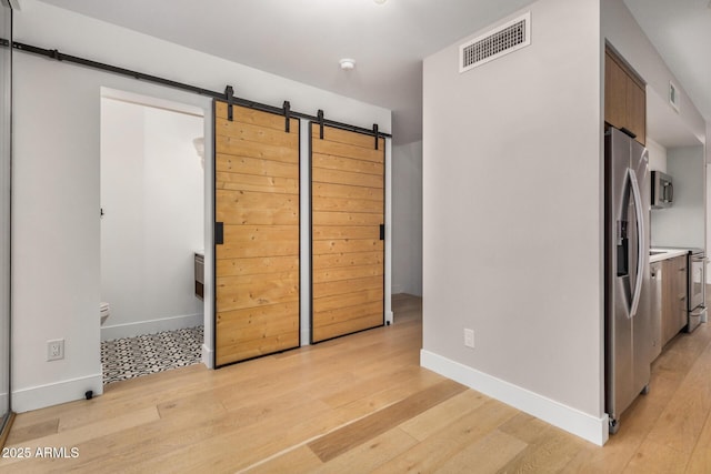 kitchen with a barn door, stainless steel appliances, visible vents, light countertops, and light wood-type flooring