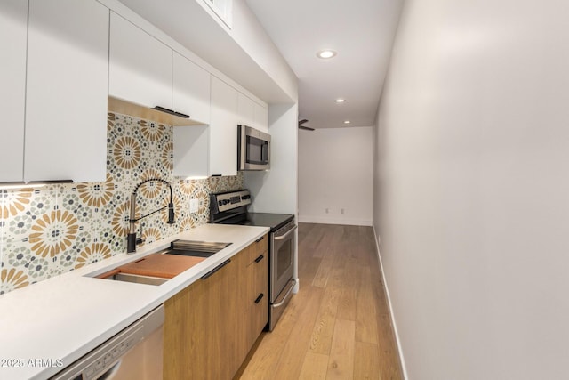 kitchen featuring a sink, light countertops, appliances with stainless steel finishes, backsplash, and modern cabinets