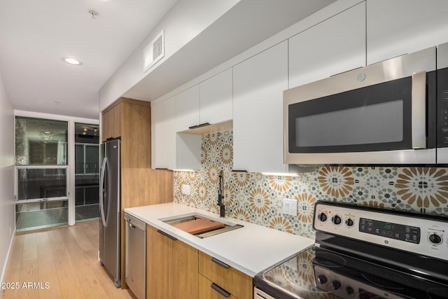 kitchen with stainless steel appliances, light countertops, visible vents, a sink, and modern cabinets