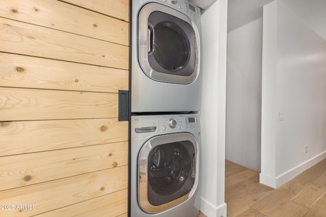 washroom with stacked washer and dryer, light wood-type flooring, laundry area, and baseboards