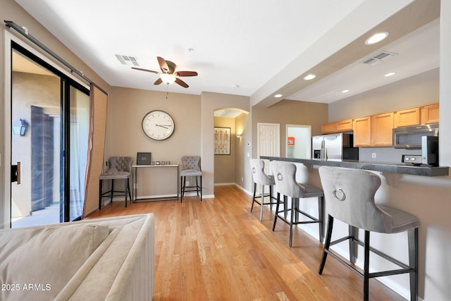 16600 N Thompson Peak Pkwy Unit 2006, Scottsdale, AZ 85260 - kitchen featuring appliances with stainless steel finishes, light brown cabinetry, a kitchen breakfast bar, arched walkways, and dark countertops