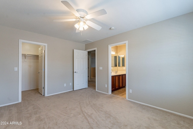 unfurnished bedroom with a walk in closet, connected bathroom, a closet, ceiling fan, and light colored carpet