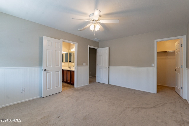 unfurnished bedroom with ensuite bath, a spacious closet, a closet, ceiling fan, and light colored carpet