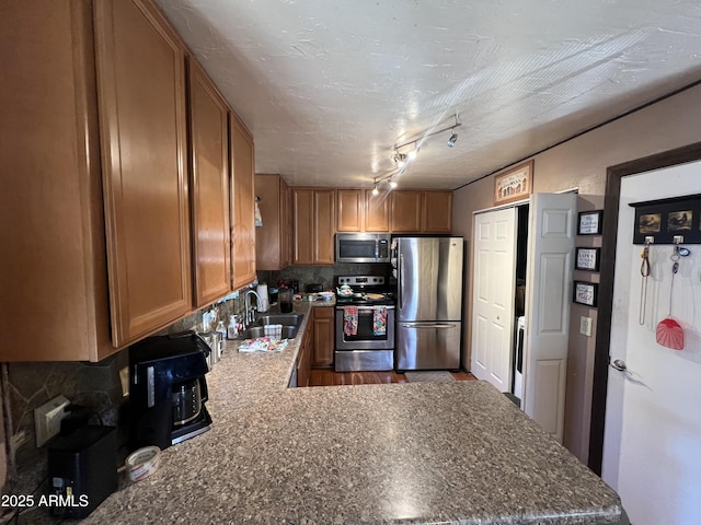 kitchen with sink, kitchen peninsula, track lighting, decorative backsplash, and appliances with stainless steel finishes