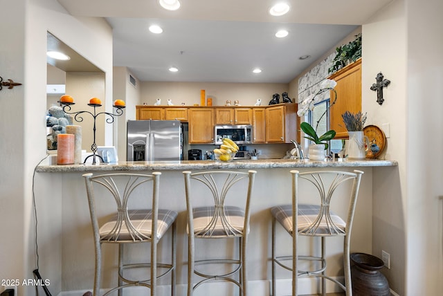 kitchen featuring appliances with stainless steel finishes, a breakfast bar, light stone countertops, and kitchen peninsula