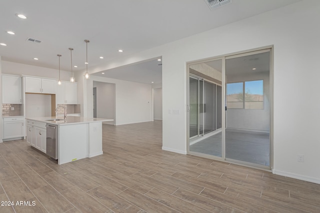 kitchen with white cabinets, hanging light fixtures, an island with sink, stainless steel dishwasher, and light wood-type flooring